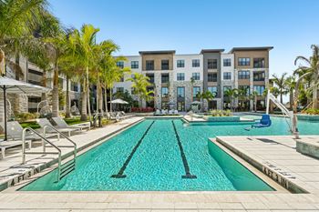 A swimming pool in front of a building with palm trees.